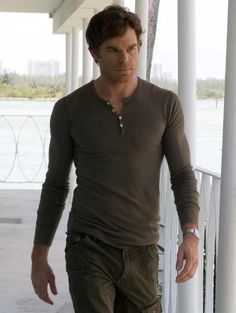 a man in brown shirt and pants walking down a porch next to a building with white pillars