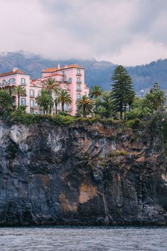 a large building sitting on top of a cliff next to the ocean with palm trees