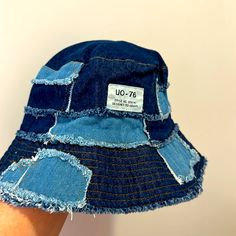 a person's hand holding up a blue jean bucket hat with patches on it