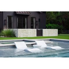 two white lounge chairs sitting on top of a swimming pool next to a house with grass