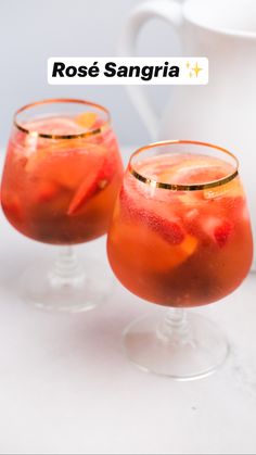 two glasses filled with red sangria on top of a white table next to a pitcher