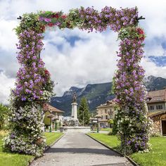 an archway with flowers on it is in the middle of a road that leads to some houses