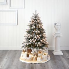 a small christmas tree with presents under it on the floor in front of a white wall