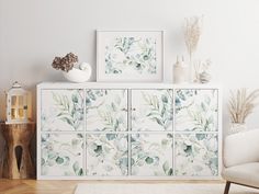 a white cabinet with green leaves painted on the doors and drawers in a living room