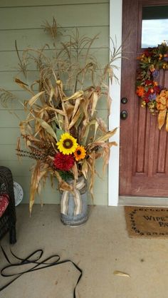 a front door with a vase full of sunflowers and corn on the porch