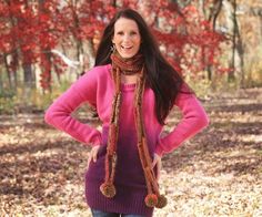 a woman standing in the woods wearing a pink sweater and scarf