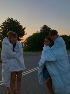 three girls wrapped in blankets walking down the street at sunset or dawn with their arms around each other