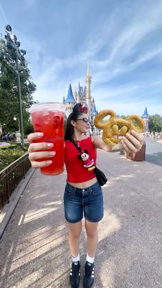 a woman holding up two pretzels and a drink in front of a castle