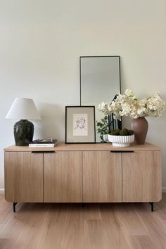 a vase with flowers on top of a wooden table next to a mirror and lamp