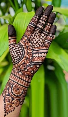 a woman's hand with henna tattoos on it and green leaves in the background