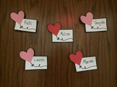 four pieces of paper with hearts and name tags attached to them on a wooden surface