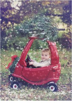 a little boy driving a red car with a christmas tree on the roof and steering wheel