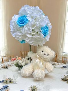 a white teddy bear sitting on top of a table with blue flowers in it's head