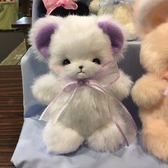 two stuffed animals sitting next to each other on a blue cloth covered chair with pink bows