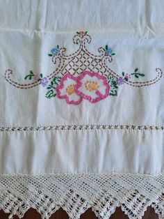 an embroidered tablecloth with flowers and lace on it's edge, sitting on a wooden surface