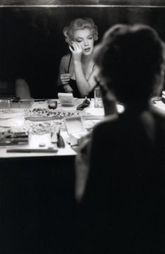 a woman sitting at a desk talking on a cell phone while looking in the mirror