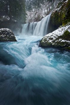 the water is rushing down the rocks in the river and there are snow on the ground