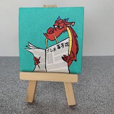 an easel with a painting of a red dragon reading a newspaper on it's side