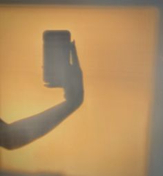 the shadow of a person's hand holding a cell phone in front of a yellow wall