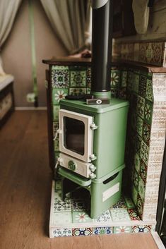 a green stove sitting on top of a wooden floor next to a wall covered in tiles