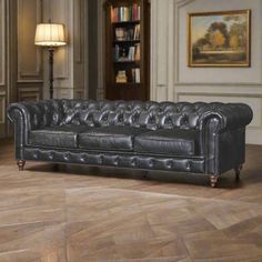 a black leather couch sitting on top of a wooden floor next to a book shelf