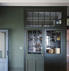 a kitchen with green walls and two doors that have glass panels on the front door