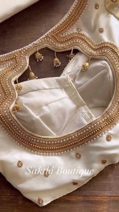 a white blouse with gold beading on the neck and bottom, sitting on a wooden floor