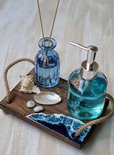 a wooden tray topped with two bottles and soap dispensers next to seashells