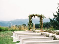 a row of white benches sitting on top of a grass covered field next to a forest