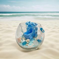 a glass bowl filled with blue items on the beach