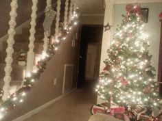 a decorated christmas tree in the corner of a room with stairs and lights on it