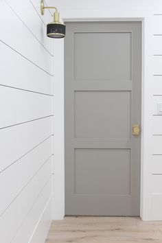 a gray door in a white room next to a light fixture and wood flooring