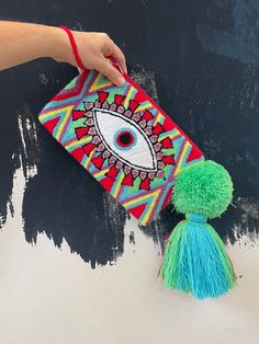 a hand holding a colorful bag with an eye on it and a green tassel