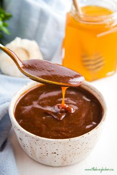 a spoon full of sauce being held over a bowl filled with brown liquid and vegetables in the background