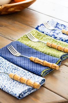 four napkins with bamboo forks on them sitting on a wooden table next to a bowl of oranges