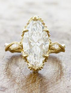 an oval shaped diamond ring on top of a wooden table with gold trimmings