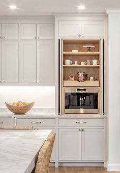 a kitchen filled with lots of white cabinets and counter top space next to a bowl of fruit