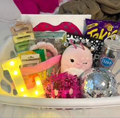 a white basket filled with lots of different types of items and lights on top of a bed