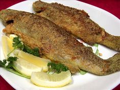 two fish on a plate with lemon wedges and parsley