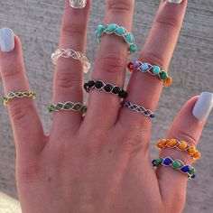 a woman's hand with five different colored rings on her fingers and one holding the other