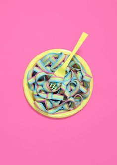 a yellow bowl filled with colorful noodles on top of a pink surface