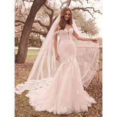 a woman wearing a wedding dress and veil posing for a photo in front of some trees