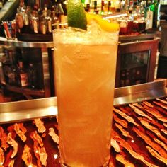 a tall glass filled with ice and lemon on top of a table next to a bar