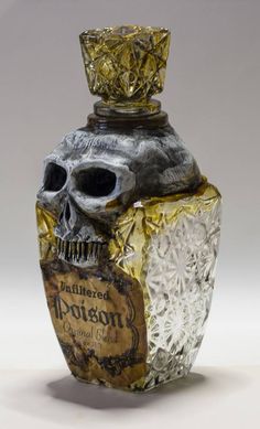 a glass bottle with a skull head on it's top and the bottom is covered in gold foil