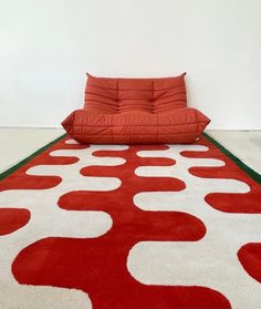 a red couch sitting on top of a white floor next to a rug covered in circles