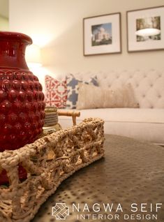 a red vase sitting on top of a wooden table next to a white couch in a living room