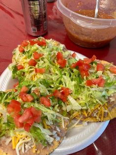 two pizzas with lettuce, tomatoes and cheese are on a paper plate