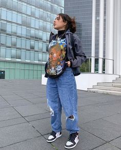 a woman standing in front of a building with her back to the camera, wearing ripped jeans and a backpack