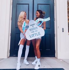 two beautiful women standing next to each other in front of a door holding signs that say hugs kisses from my little