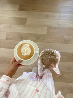 a person holding a cup of coffee on top of a wooden floor next to a white plate